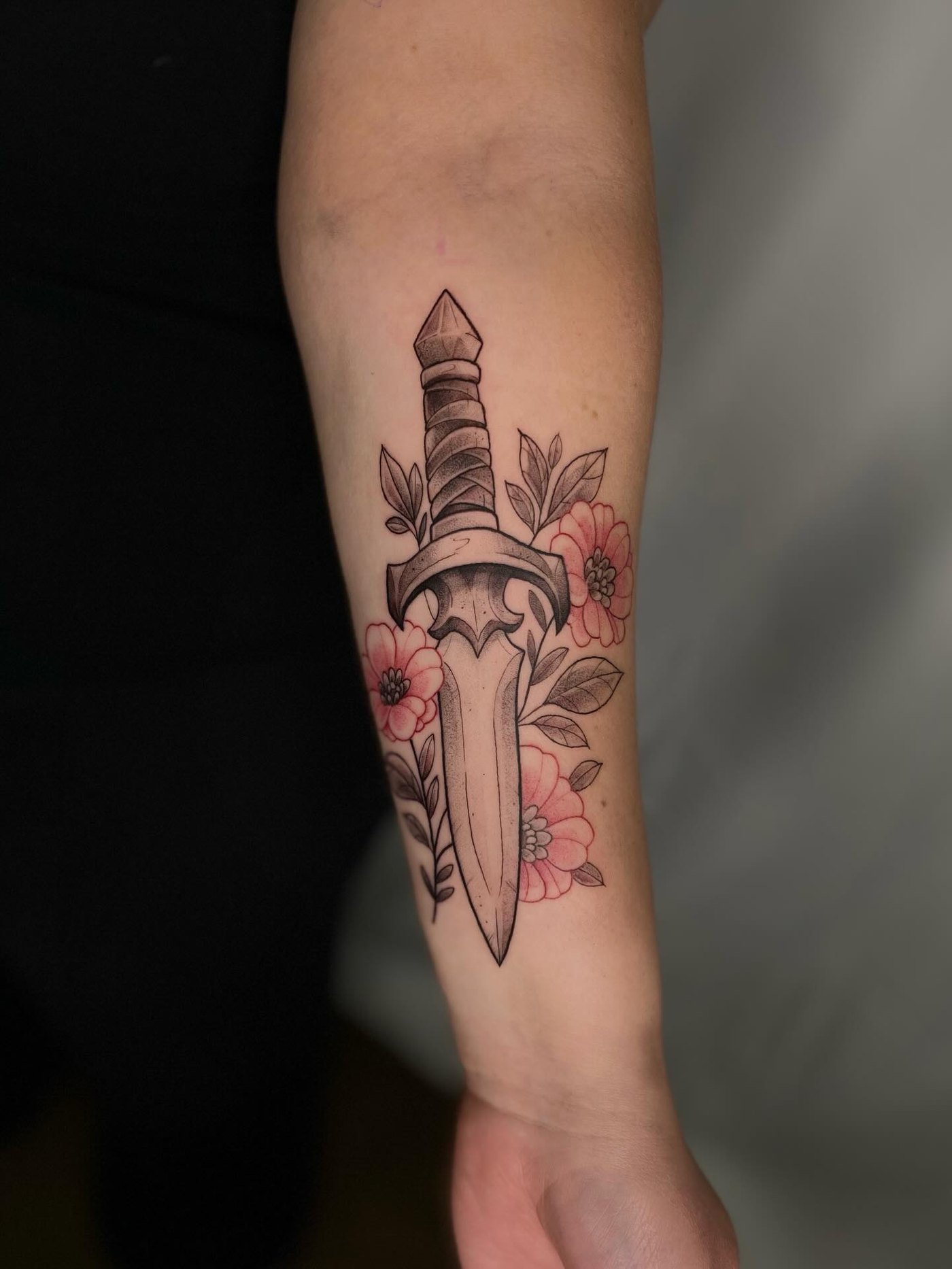 Tatouage d'une dague entourée de fleurs sur l'avant-bras
